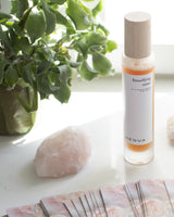 Skincare bottle labeled 'Henua' on a surface with a plant and rose quartz rock in the background