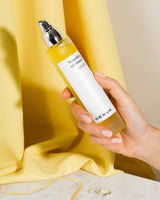 Hand holding a bottle of Henua oil cleanser against a yellow fabric background