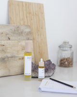 Two skincare bottles labeled 'henua' on a surface with a notebook and pen, and a wooden cutting board in the background.