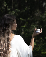 Woman holding a Henua Microbiome mask with green nature in the background