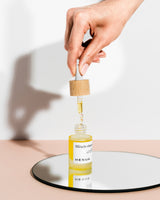 Hand holding a dropper over a bottle labeled 'Miracle Vitamin' by Henua on a reflective surface.