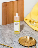 Bottle of HENUA skincare The Pauser bio retinol serum product on a marble surface with a wooden board and yellow pouch in the background.