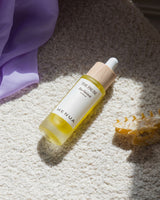 HENUA The Pause bio-retinol serum bottle on a textured surface with a purple towel and hairbrush in the background